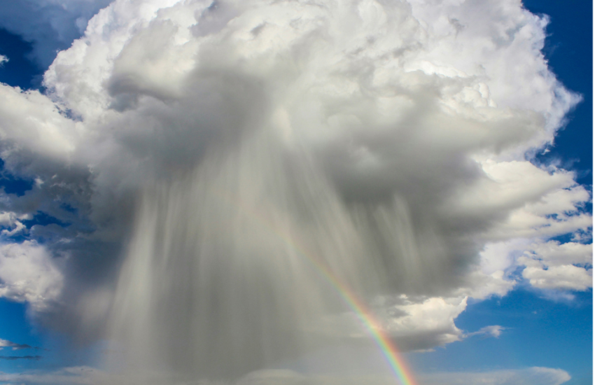 large cloud in the sky with rain pouring out of it and a rainbow off to the side.